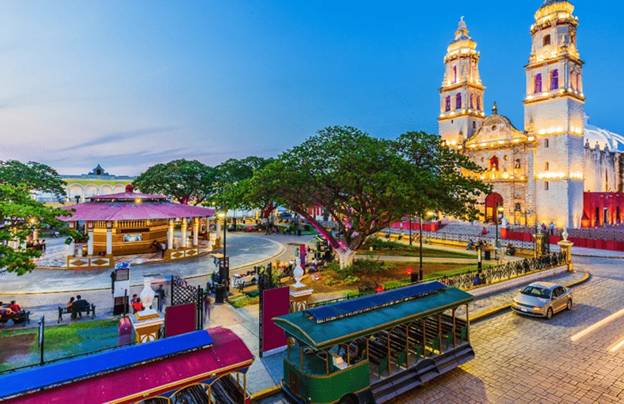 The Main Square of Campeche, Mexico at dusk. In the background, the Cathedral of Our Lady of the Immaculate Conception is lit up.