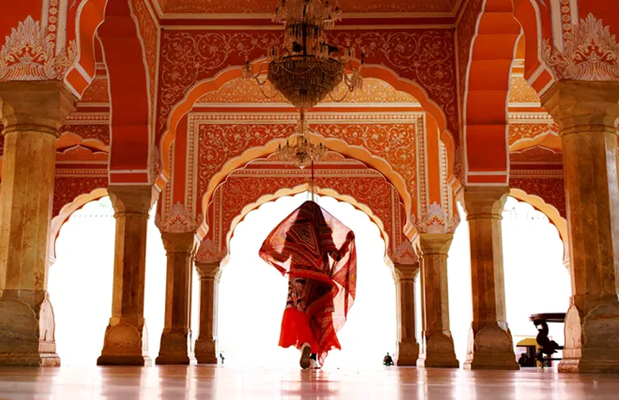 Interior of City Palace in Jaipur, India. In the center, a woman faces away from view, walking through the corridor.