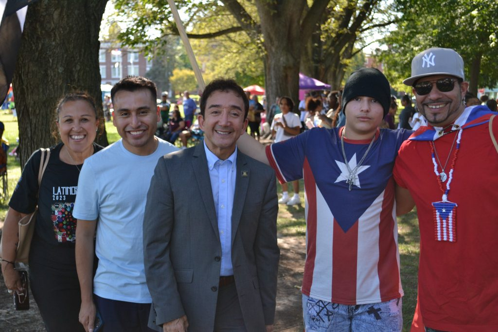 A smiling group of people at an outdoor event, with one person wearing a Puerto Rican flag shirt.