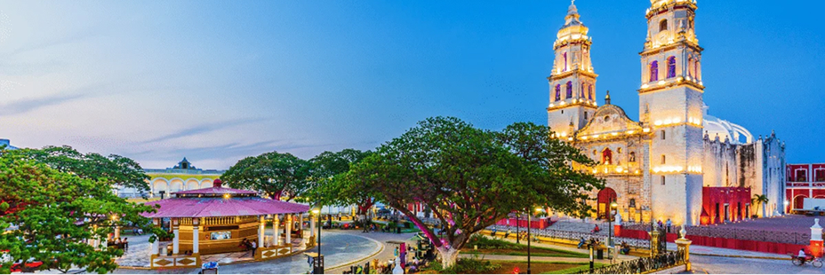 The Main Square of Campeche, Mexico at dusk. In the background, the Cathedral of Our Lady of the Immaculate Conception is lit up.