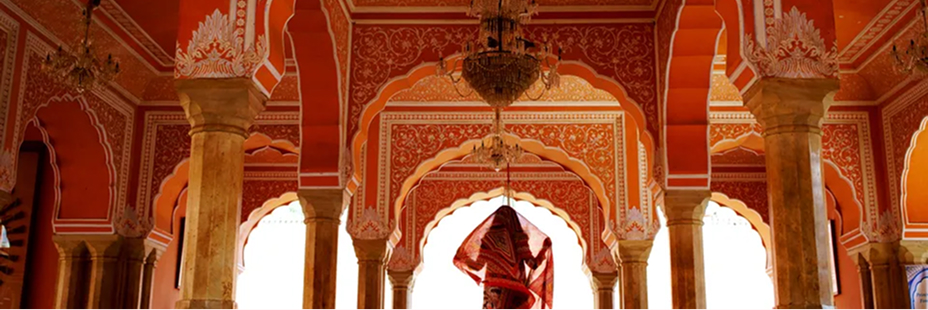 Interior of City Palace in Jaipur, India. In the center, a woman faces away from view, walking through the corridor.