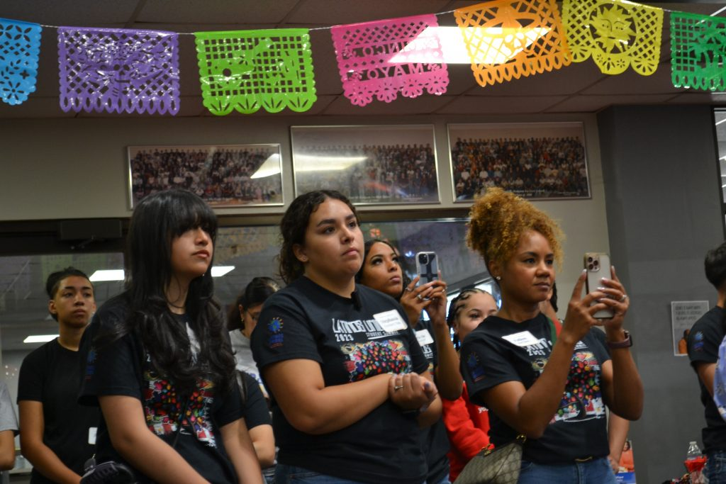 A group of young people at a Latinos United summit listening intently under colorful festive banners.